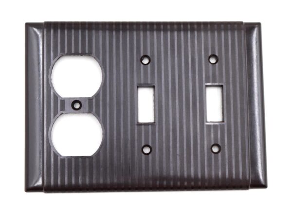 Vintage brown Bakelite two-gang wall plate with a duplex outlet cutout, two switch openings, and four screw holes, shown front on.