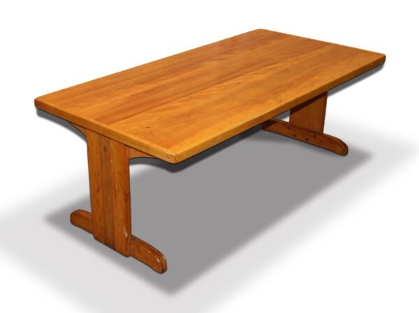 Wood coffee table with a rectangular top and trestle base shown at an angle, featuring a medium wood tone and visible surface wear.