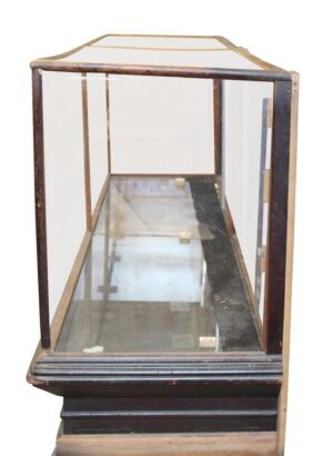 Antique glass-front showcase with an oak frame, clear glass panels, and a beveled black base, shown with an open side and visible wear from prior restoration.