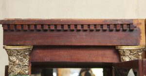 Close-up of a built-in display cabinet with dentil molding and foliate carved pillars, showing the upper wood surround and decorative bracket details.