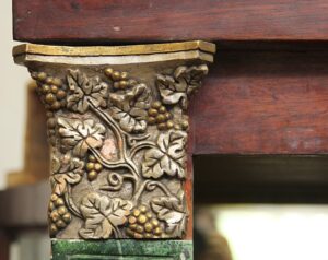 Close-up of a built-in display cabinet corner with an antique brass foliate capital beneath dark wood molding.