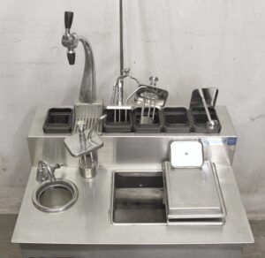 Vintage ice cream and soda fountain machine with multiple labeled flavor lids, a tall draft arm, and a sink basin, shown in a front view with surface wear visible.