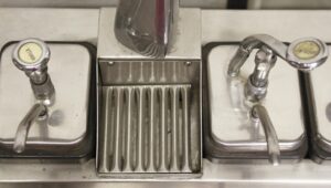 Close-up of a vintage ice cream machine center showing the vanilla and chocolate lid handles and the central draft arm.