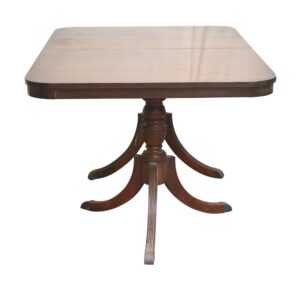 Regency Revival drop leaf dining table in dark wood tone with a rectangular top and a carved pedestal base with curved saber legs.