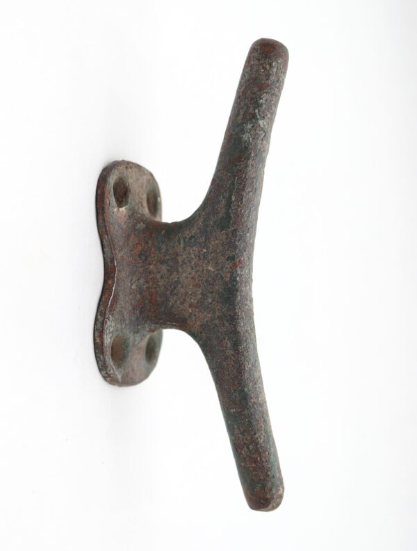 Vintage cast iron cleat wall hook with distressed green paint and two mounting holes, shown in close-up.