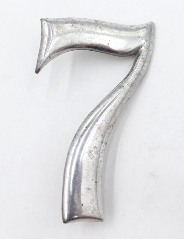 Vintage aluminum house number seven with a curved form and visible surface wear.