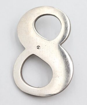 Vintage brushed steel house number 8 with surface wear and two mounting prongs on the back.