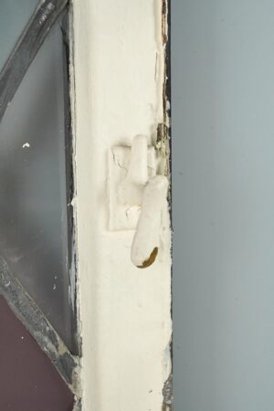 Close-up of a Tudor-style casement window showing the white-painted steel frame, original hinge hardware, and leaded stained glass edge.