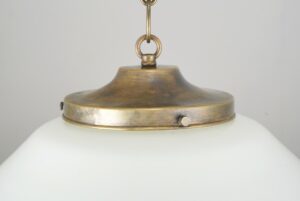 Close-up of a schoolhouse pendant light showing the antique brass fitter and chain attachment above the milk glass globe.