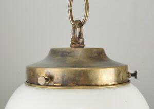 Close-up of a schoolhouse pendant light showing the antique brass chain fitter, hanging ring, and the top of the milk glass globe.