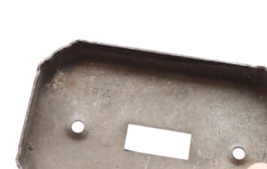Close-up of a distressed black steel toggle switch cover wall plate with two mounting holes and heavy surface wear.
