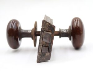 Antique brown ceramic door knob set with a cast iron rim lock and spindle, shown from the side with surface wear visible.