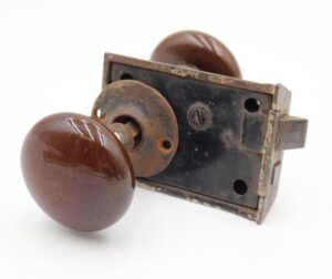 Antique door knob set with brown ceramic knobs, a cast iron rim lock, and a rosette, shown in a close-up view with surface wear and rust.