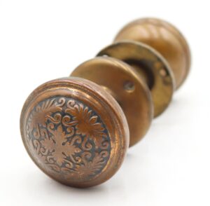 Antique brass passage door knob with an ornate floral front face and three matching knob sections shown in close-up.