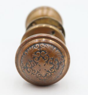 Antique brass door knob with an ornate floral rosette pattern viewed from the end.