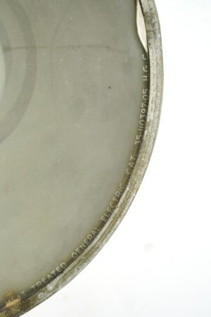Close-up of a green industrial floodlight lens and worn metal rim with partial General Electric markings.