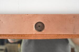 Close-up of a copper mirror frame with a round recessed detail and wood trim along the bottom edge.