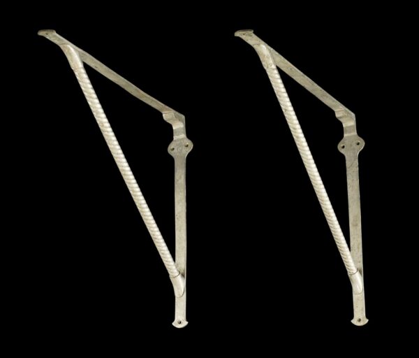 Pair of shelf brackets shown side by side, each with a twisted rope support bar and mounting holes, one slightly bent.