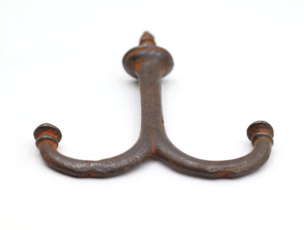 Vintage cast iron double arm ceiling mount hook with a screw top and two curved arms, shown in a close-up view with visible surface wear and rust.