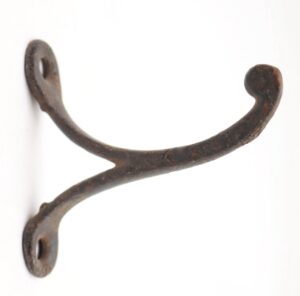 Single-arm cast iron wall hook with a ball tip and two mounting holes, shown in close-up with heavy surface wear and rust.