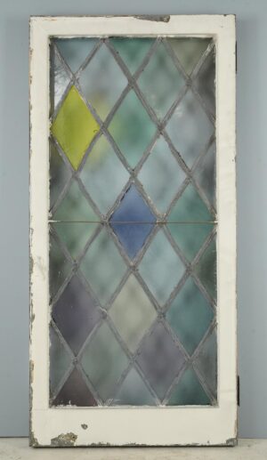 Tudor-style casement window with a leaded diamond stained glass pattern in pastel colors, shown in a worn white frame with the hinge visible on one side.