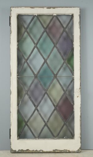 Tudor-style casement window with a leaded diamond stained glass pattern, showing the white side of the steel frame, attached hinges, and visible surface wear.