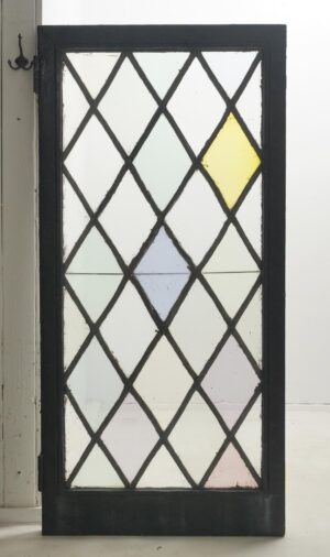 Tudor-style casement window with a leaded diamond stained glass pattern, shown in a black steel frame with visible hinges and a few pastel-colored panes.