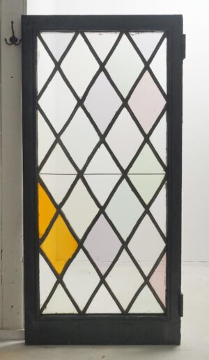 Tudor-style casement window with a leaded diamond stained glass pattern, black-painted steel frame, and visible surface wear, shown with the right-side hinges attached.