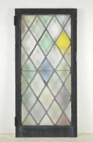 Tudor-style casement window with a leaded diamond stained glass pattern in pastel colors and a black-painted steel frame.