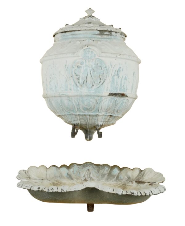 French-style enameled cast iron wall fountain shown as two pieces, with a lidded upper reservoir and a scallop-shaped lower basin in pale blue and white with visible wear.