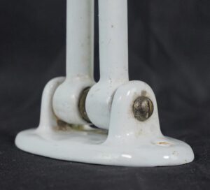 Close-up of a white enamel cast iron towel rack showing the double arm pivot and one mounting screw, with minor wear visible on the hardware.