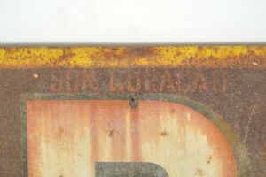 Close-up of a vintage French Picon advertising sign with worn enamel, rust, and a partially visible orange and gray graphic.