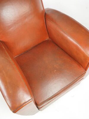 Close-up of a brown leather club chair seat and armrest with visible wear and age marks.