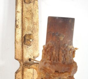 Close-up of a gilt wrought iron wall sconce with a textured candle sleeve and part of the scrollwork visible.