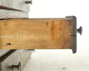 Close-up of a vintage shop counter cabinet showing a dark wood drawer side with brass hardware and a metal corner bracket.