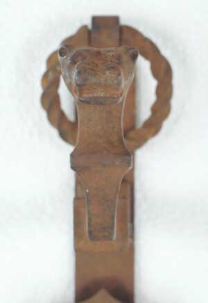 Close-up of a Gothic wrought iron door pull with a lion knocker and central shield detail, showing heavy surface wear and rust.