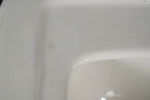 Close-up of a white porcelain sink basin with visible surface wear and staining.