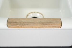 Close-up of a white porcelain utility sink basin with a worn light wood strip protecting the front rim.