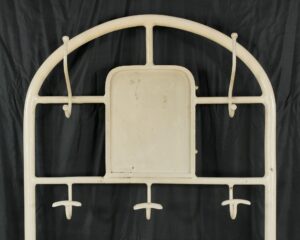 Vintage white enamel steel hall tree with arched frame, central panel, five hooks, and surface wear visible.