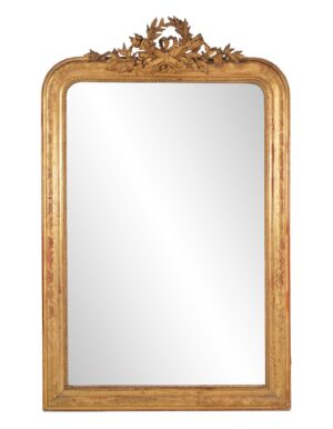 Antique Louis Philippe wall mirror with rounded upper corners, a straight bottom edge, and an ornate carved crest above the gilt frame, shown with visible age spots and surface wear.