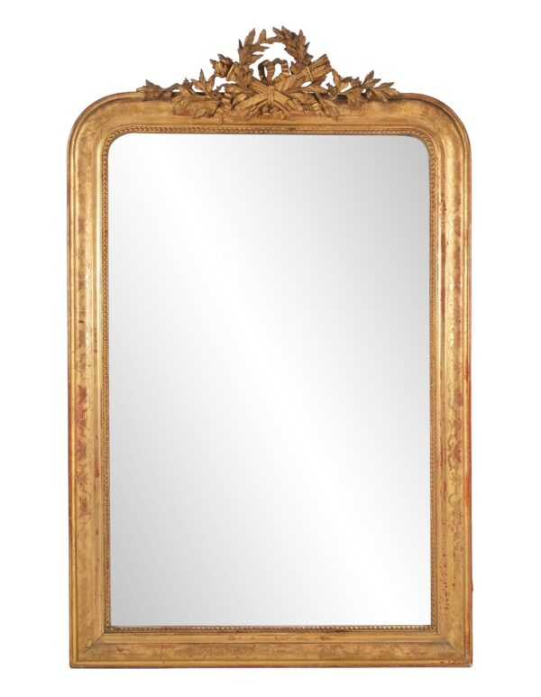 Antique Louis Philippe wall mirror with rounded upper corners, a straight bottom edge, and an ornate carved crest above the gilt frame, shown with visible age spots and surface wear.