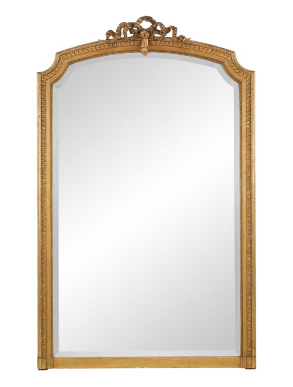 Arched wall mirror with a ribbon crest, fluted frame, and aged mirror surface.