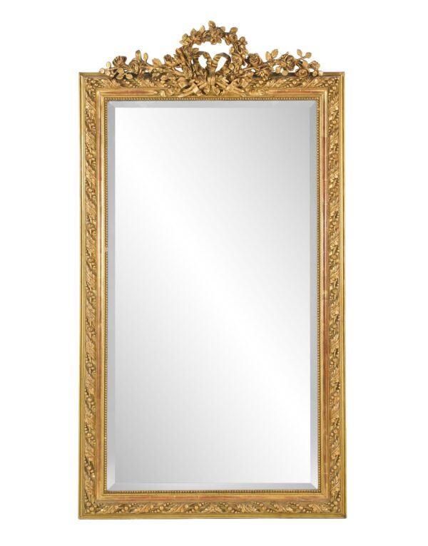 Rectangular wall mirror with an ornate giltwood frame and carved floral crest at the top, showing visible age spots on the glass.