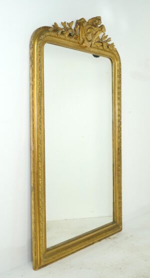 Tall giltwood mirror with rounded upper corners, a straight bottom edge, and an ornate crest at the top.