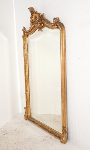 Tall Rococo wall mirror with an ornate crest, gilt frame, and visible age spots on the glass.