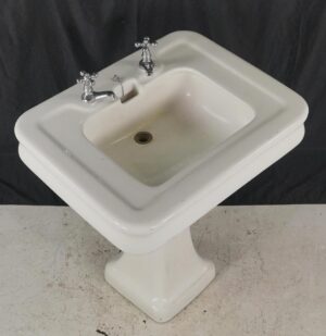 White Art Deco pedestal sink with chrome two-handle faucet and visible bowl staining.