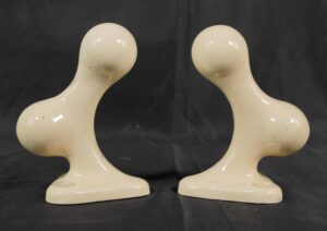 Pair of ceramic towel bar brackets with an almond porcelain finish, shown as a matching pair with curved supports and rectangular bases.