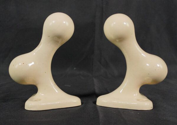 Pair of ceramic towel bar brackets with an almond porcelain finish, shown as a matching pair with curved supports and rectangular bases.