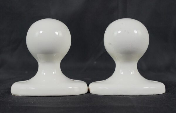 Pair of white ceramic towel bar brackets shown side by side, each with a rounded top and broad base, with visible surface wear and small chips.