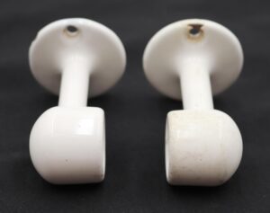 Pair of vintage white enameled cast iron towel brackets shown as a pair, with round mounting plates and curved holders, viewed from the back.